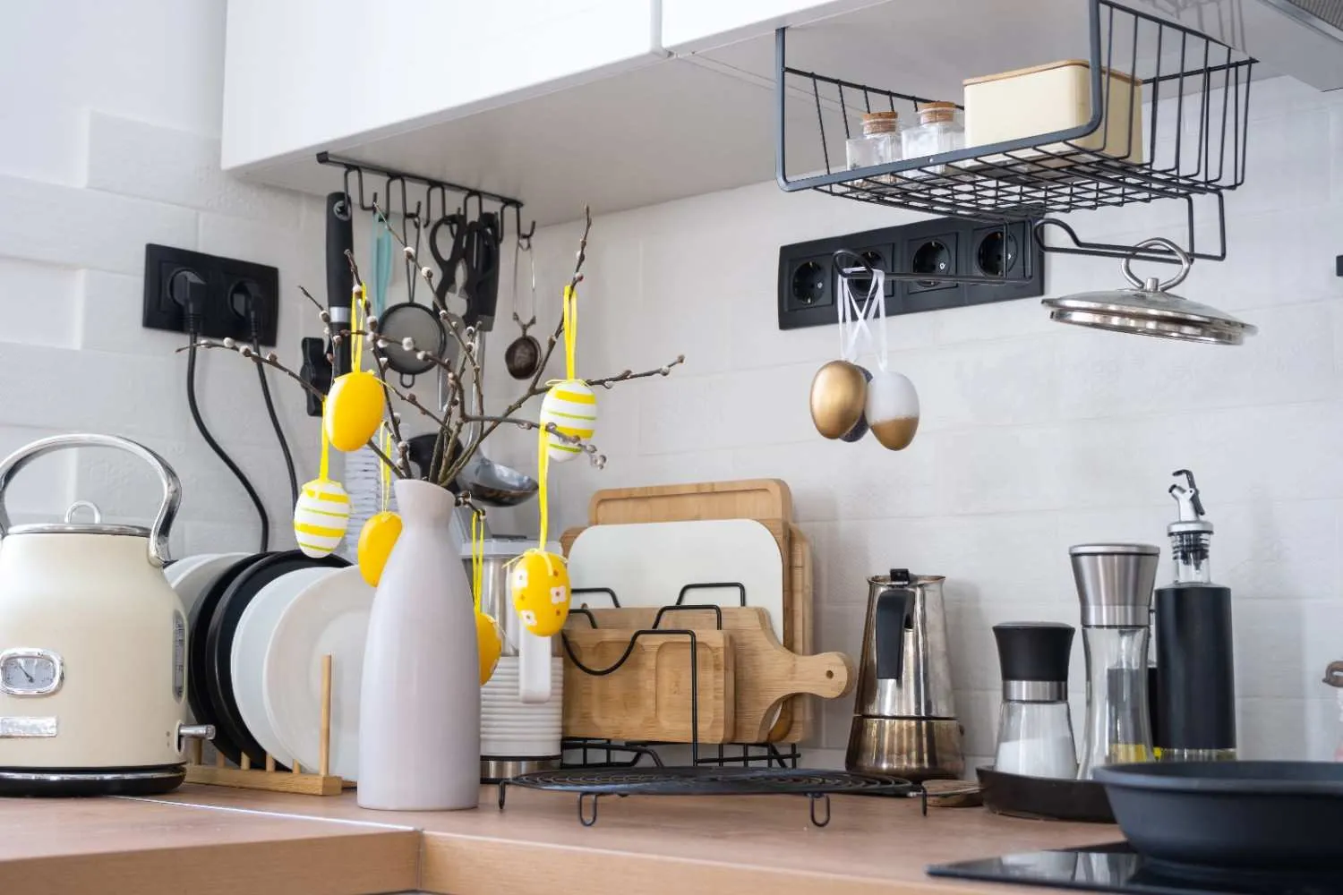 A modern white kitchen featuring an under-cabinet wire basket, a wall-mounted utensil rack, and a vertical cutting board holder on a wooden countertop.