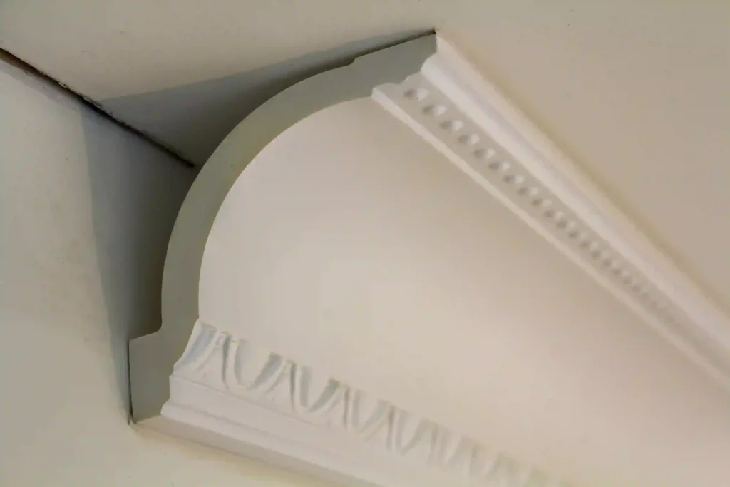 A close-up detail of white decorative ceiling crown moulding, demonstrating the precision required to determine What is a Shim's role in creating seamless joints and understanding What is Casing Moulding in 2026 home design.