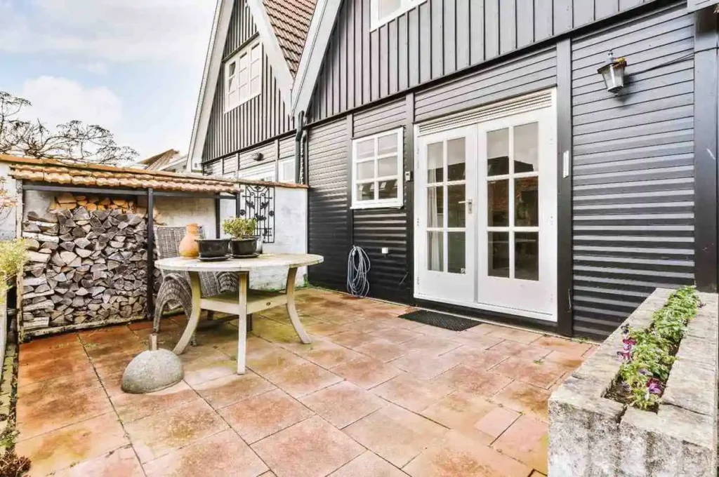 A modern 2026 Exterior Home Remodeling Ideas project featuring black horizontal siding, white-trimmed French doors, and a stone-paved patio with a built-in planter.