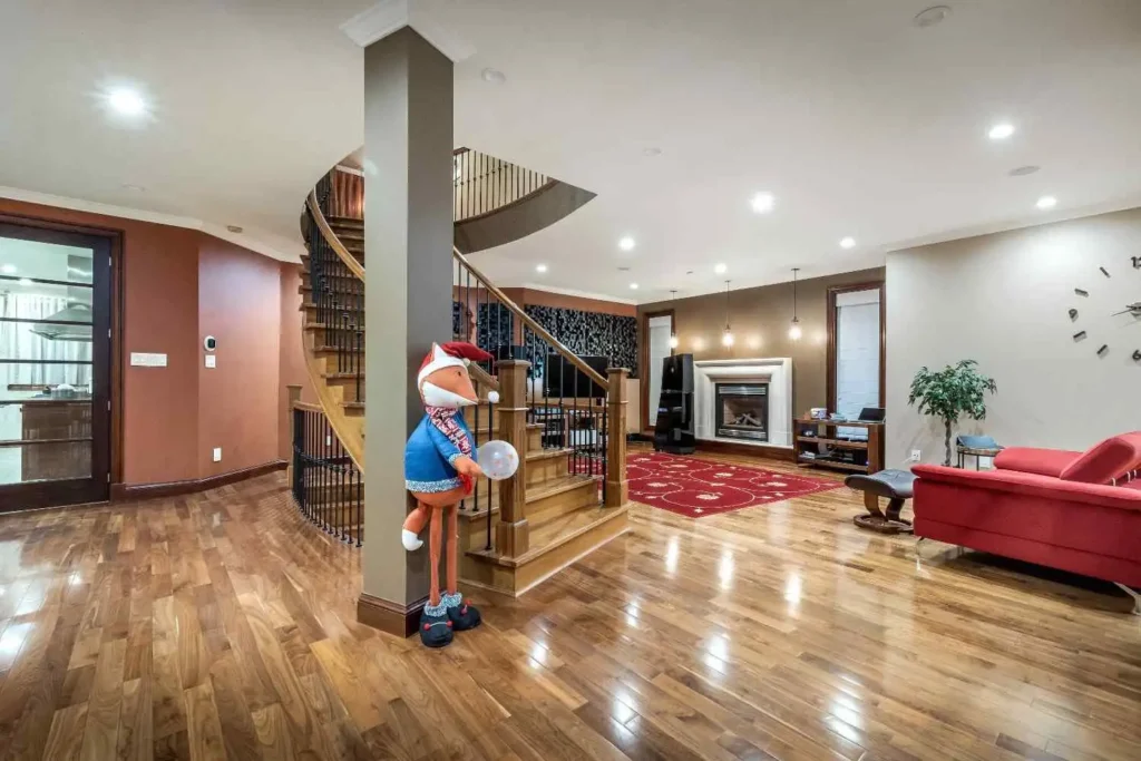 Open-concept luxury basement remodel in Rancho Santa Fe featuring a custom curved wood staircase, structural support column, and integrated home theater system.