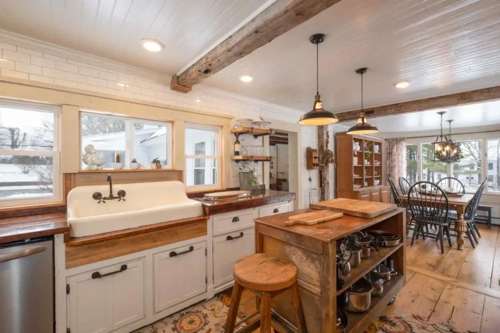 Modern farmhouse kitchen with white shaker cabinets, apron front sink, wood island, exposed ceiling beams, and pendant lighting
