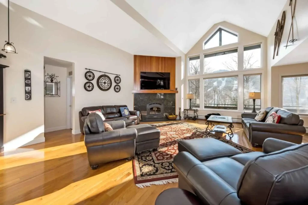 Spacious Rancho Santa Fe living room featuring vaulted ceilings, floor-to-ceiling windows with mountain views, a custom stone fireplace, and polished hardwood floors.