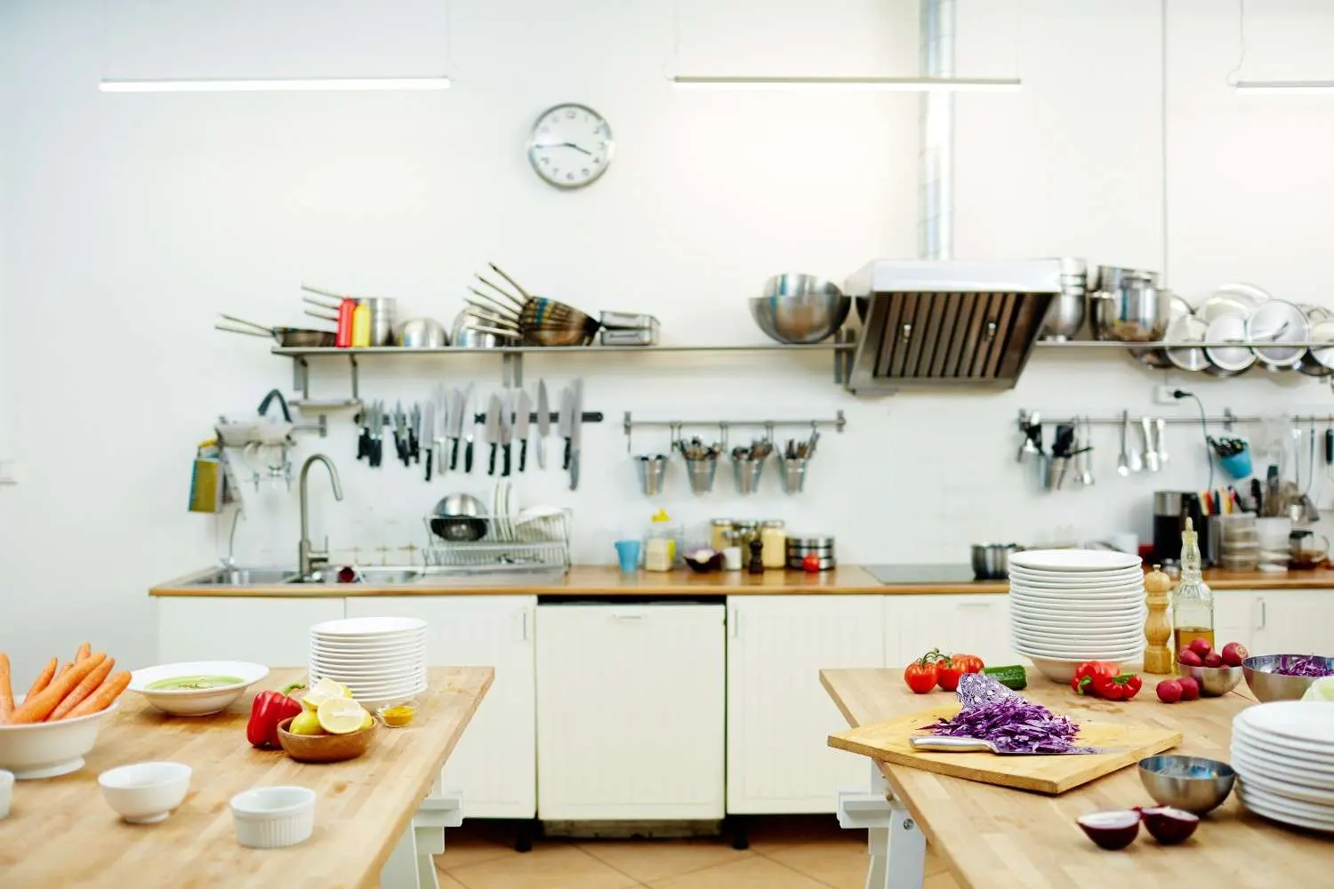 A bright, organized commercial kitchen featuring wooden prep tables with fresh vegetables, wall-mounted knife racks, and stainless steel shelving for efficient workflow.