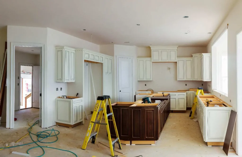 An image illustrating what to consider when renovating a kitchen, showing the installation of cabinets and a dark wood island on an active construction site.
